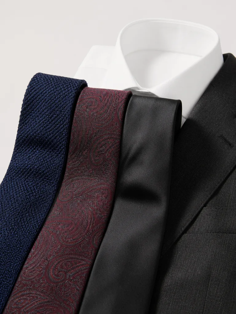 Tre slipsar i mörkblå grenadine, burgundy paisley och svart siden vid en vit skjorta och kostym i editorial fotostil